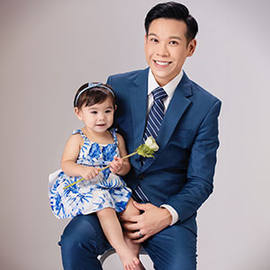 Attorney David Nguyen, wearing a blue suit, smiles while holding his daughter, who is wearing a blue and white dress. - Law Office of David Nguyen, PC.